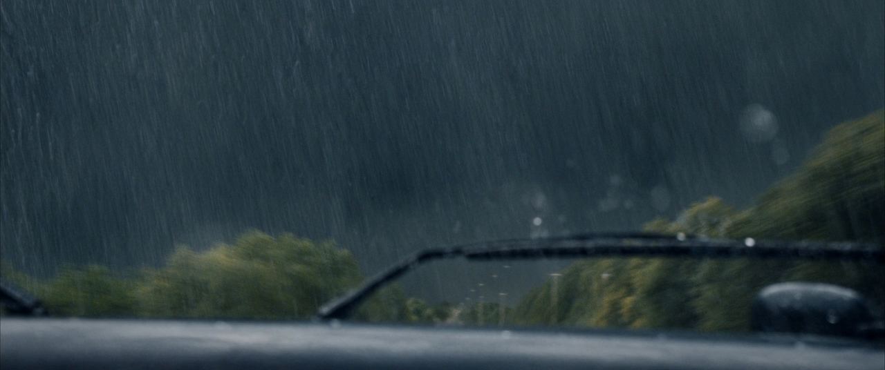 Heavy summer rain sheeting across a car windshield with wipers mid-sweep